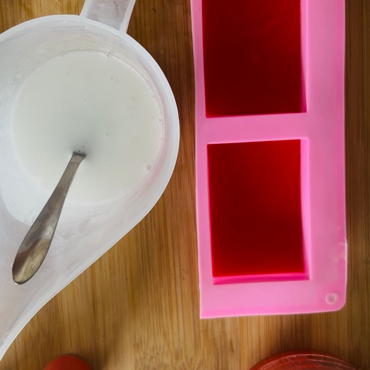 Pink silicone mold on a wooden surface with a white container and spoon.