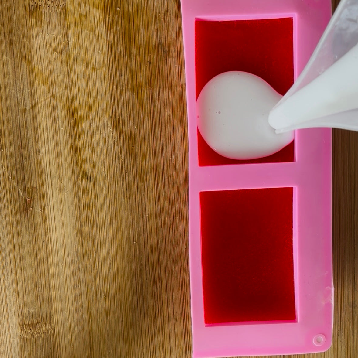 White sphere being poured into a pink silicone mold on a wooden surface